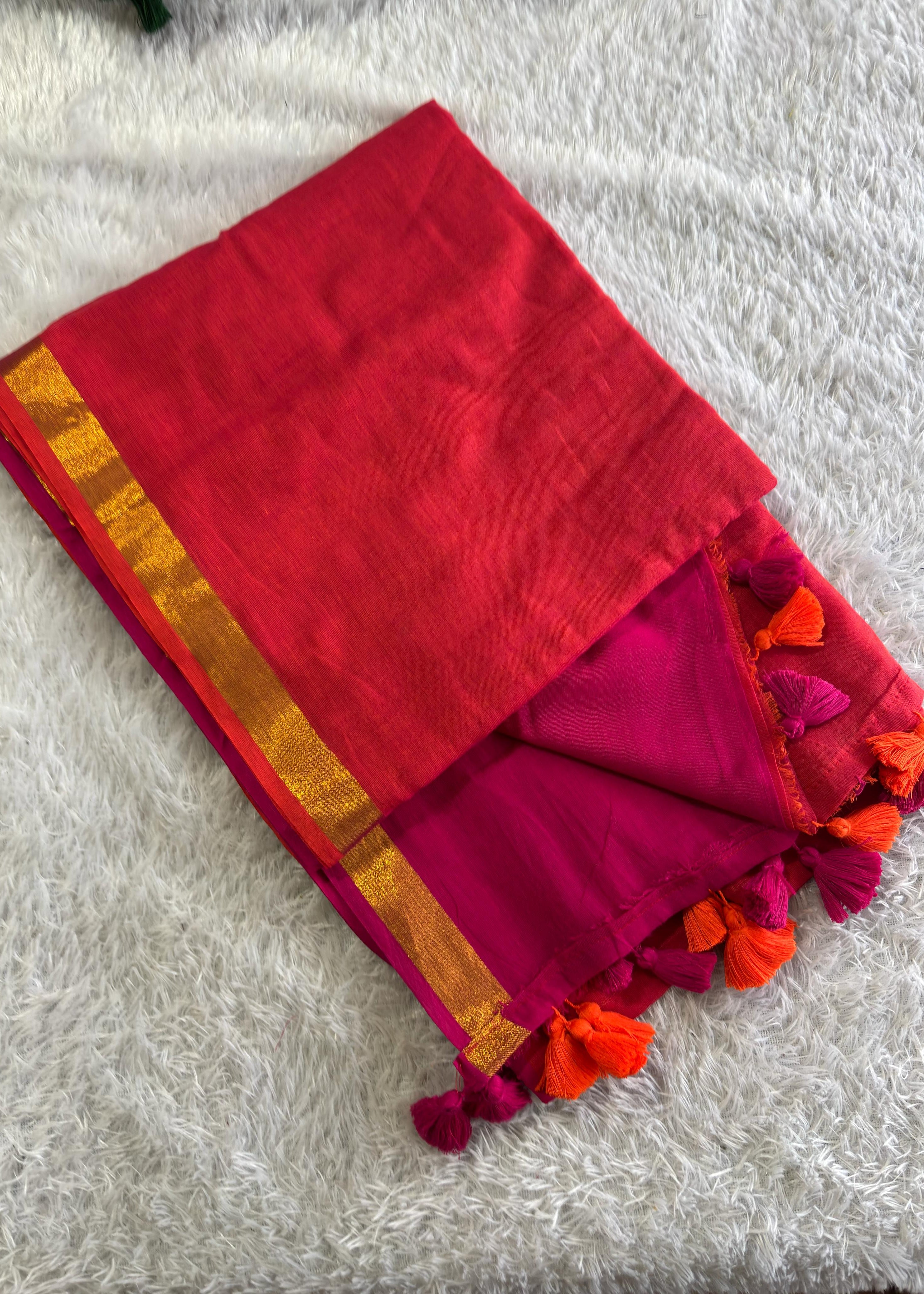 Red and pink saree with orange border and tassels on a white surface
