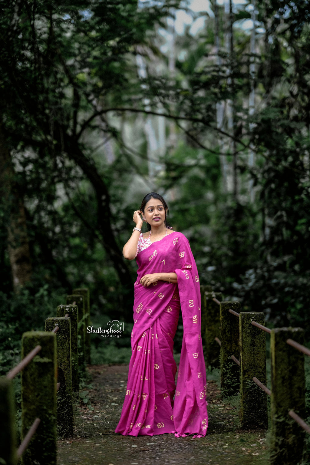 Woman in a bright pink saree standing in a forest setting
