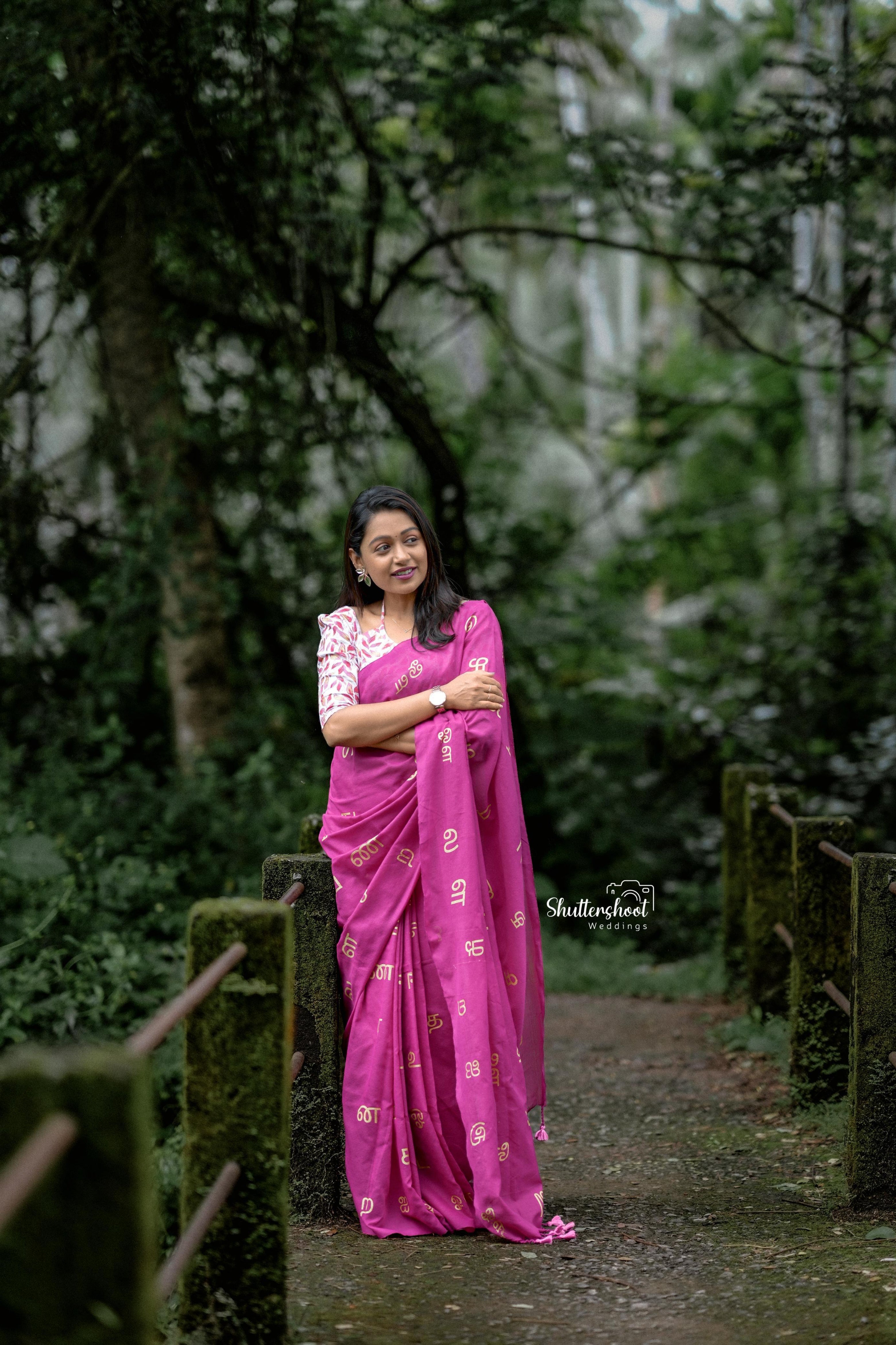 Woman in a pink saree standing in a forested area