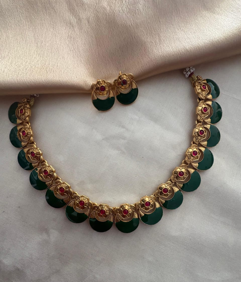 Gold necklace with green beads and red stones on a marble surface
